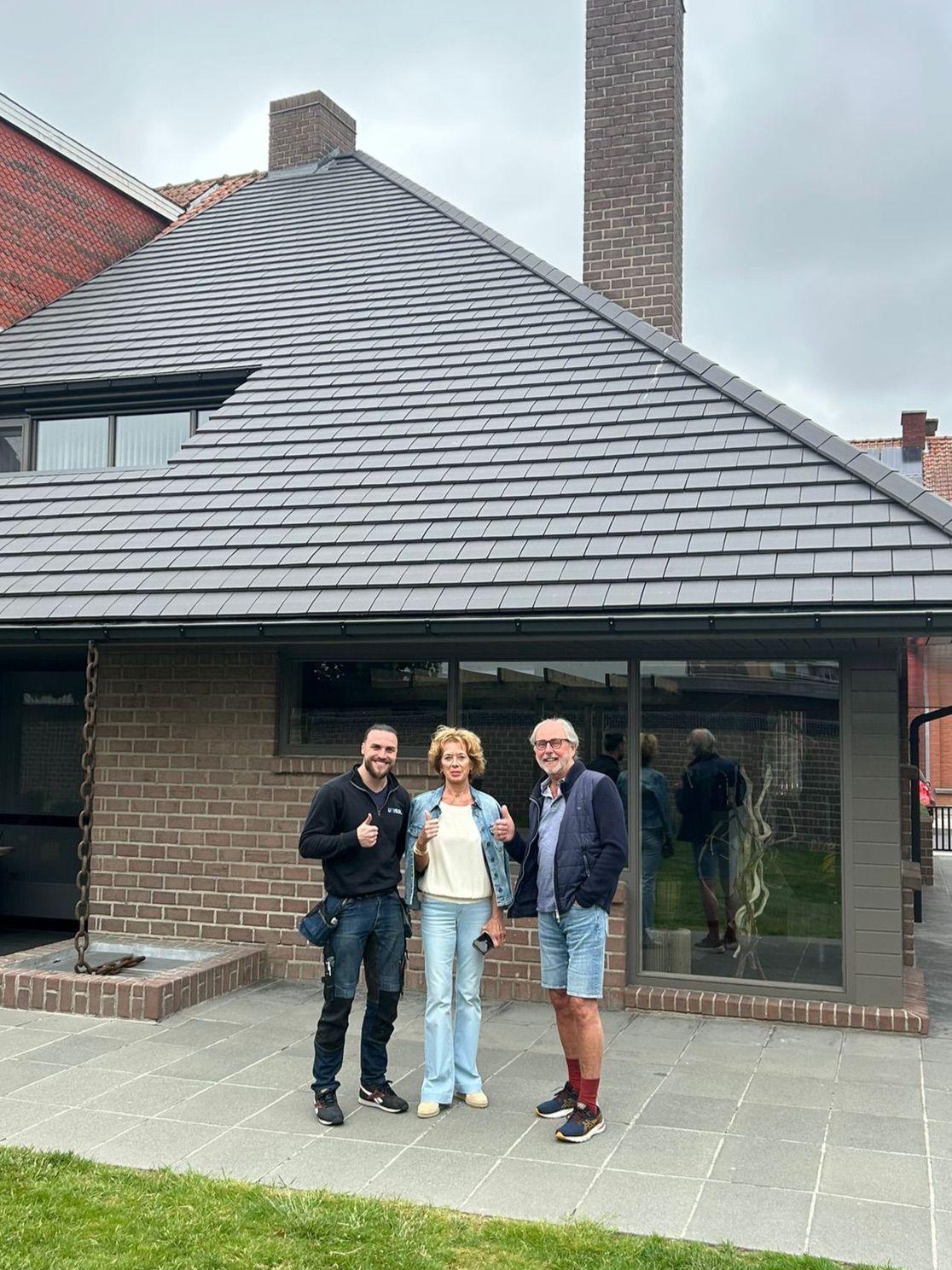 Blije klanten poseren voor hun gerenoveerde woning met nieuwe dakbedekking, geplaatst door Sellevate. Afgewerkt dakproject met modern materiaal en tevreden bewoners in beeld.